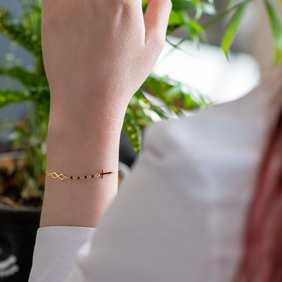 AV χρυσό γυναικείο βραχιόλι με σχέδια το άπειρο, σταυρό και μαύρες πέτρες